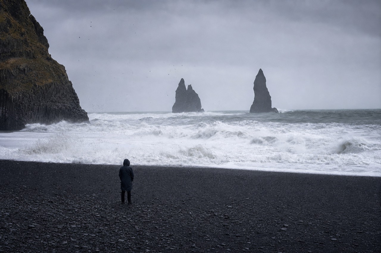 Visitors keeping a wide, safe distance from the surf line on the black sand at Reynisfjara
