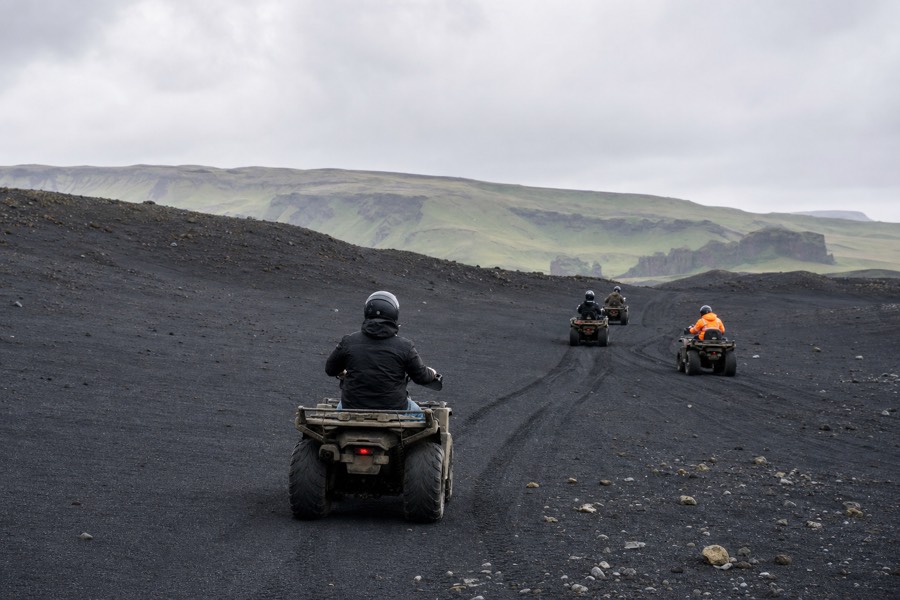 A guided quad bike tour riding across black volcanic sand dunes near Vik, Iceland