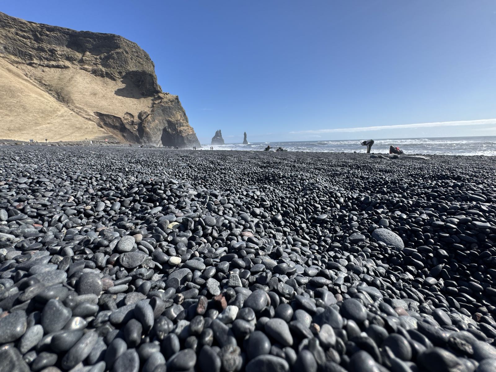 The wide black sand beach at Reynisfjara with the Reynisfjall cliff and sea stacks under a moody Iceland sky